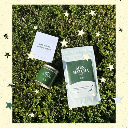A styled flat-lay of a Shin Matcha Club canister and a matching pouch placed on green foliage, with a small card in between. The scene is framed by a cream border decorated with star illustrations.